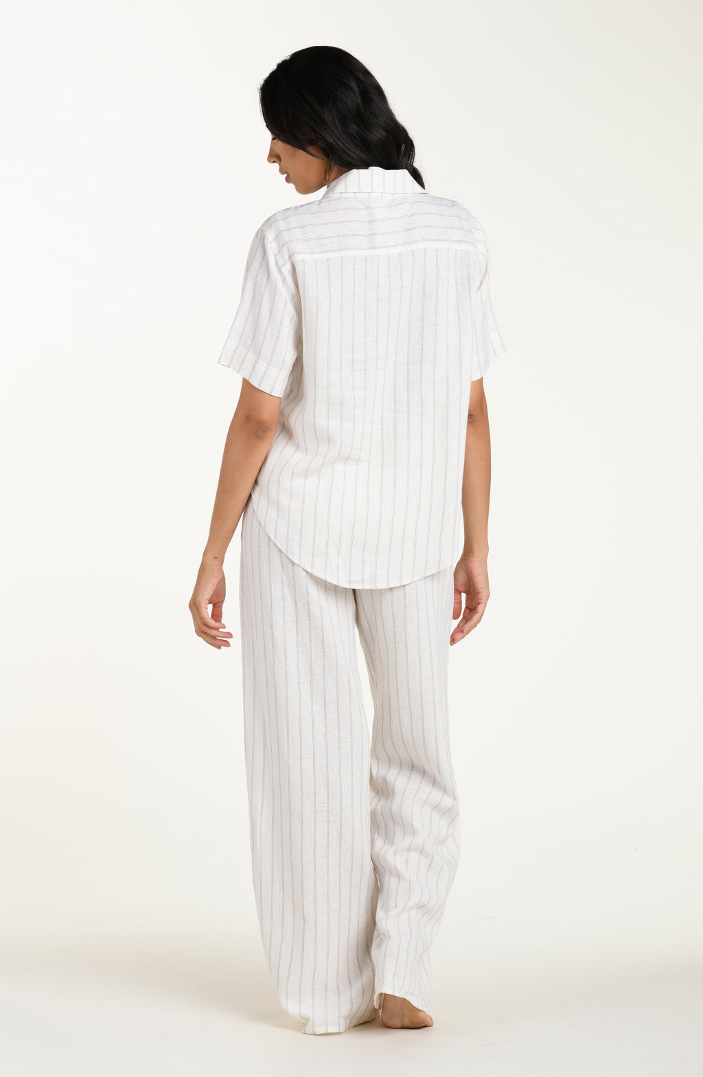Back image of model wearing a cream striped colored short-sleeve cover-up shirt with button front, chest pocket, and tie-front waist.