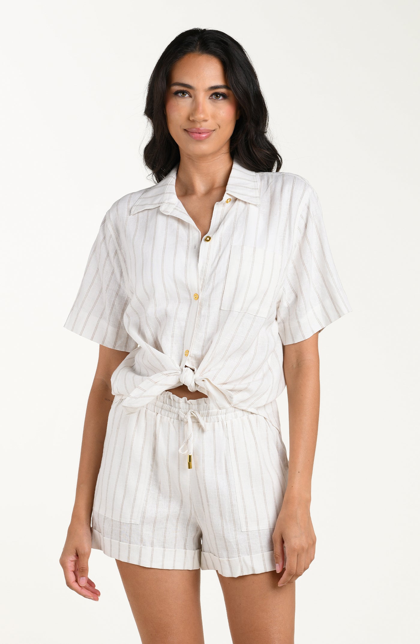 
                  
                    Front image of model wearing a cream striped colored short-sleeve cover-up shirt with button front, chest pocket, and tie-front waist. It's paired with matching beach shorts.
                  
                