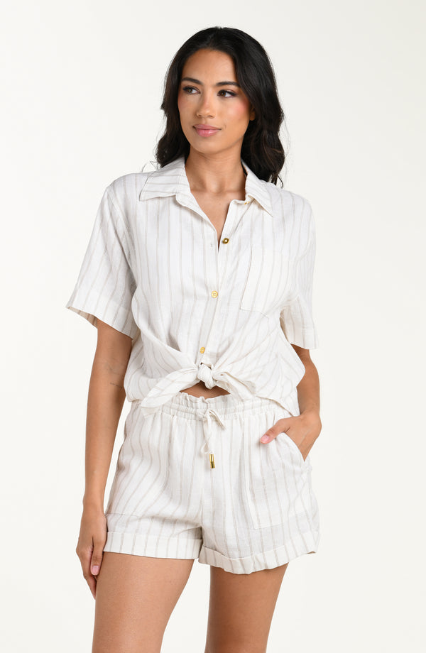 Front image of model wearing a cream striped colored short-sleeve cover-up shirt with button front, chest pocket, and tie-front waist. It's paired with matching beach shorts.