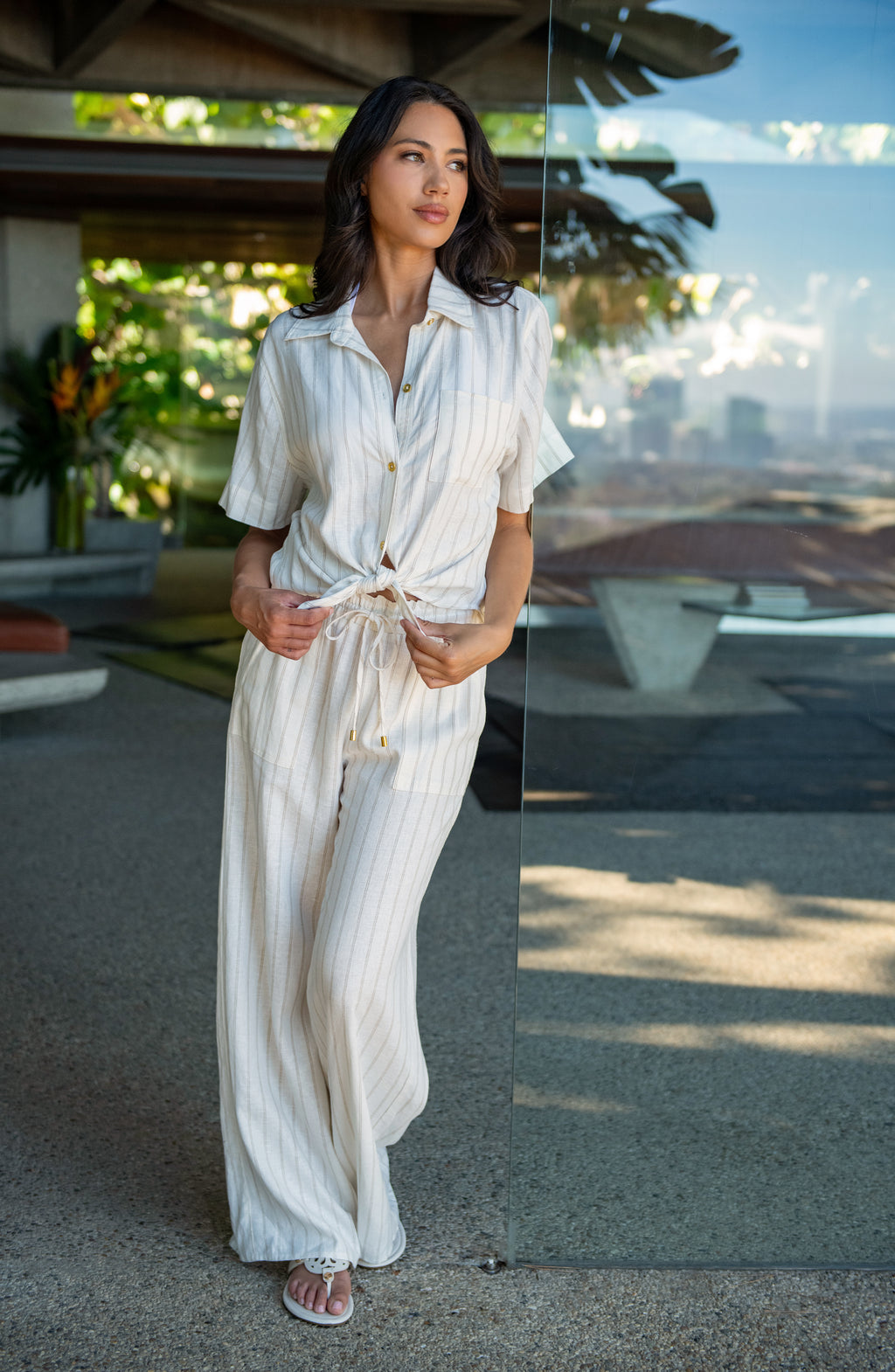 Lifestyle image of model wearing a cream striped colored wide-leg beach pants with a relaxed fit, drawstring waistband, and pockets.