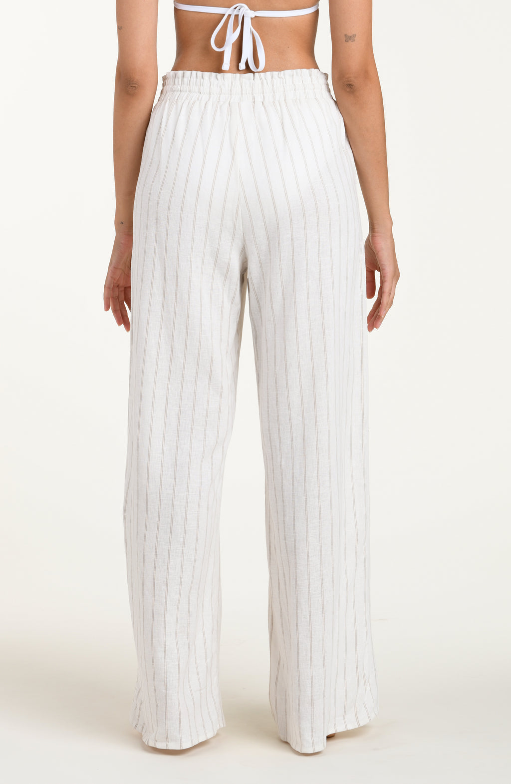 Back image of model wearing a cream striped colored wide-leg beach pants with a relaxed fit, drawstring waistband, and pockets. 