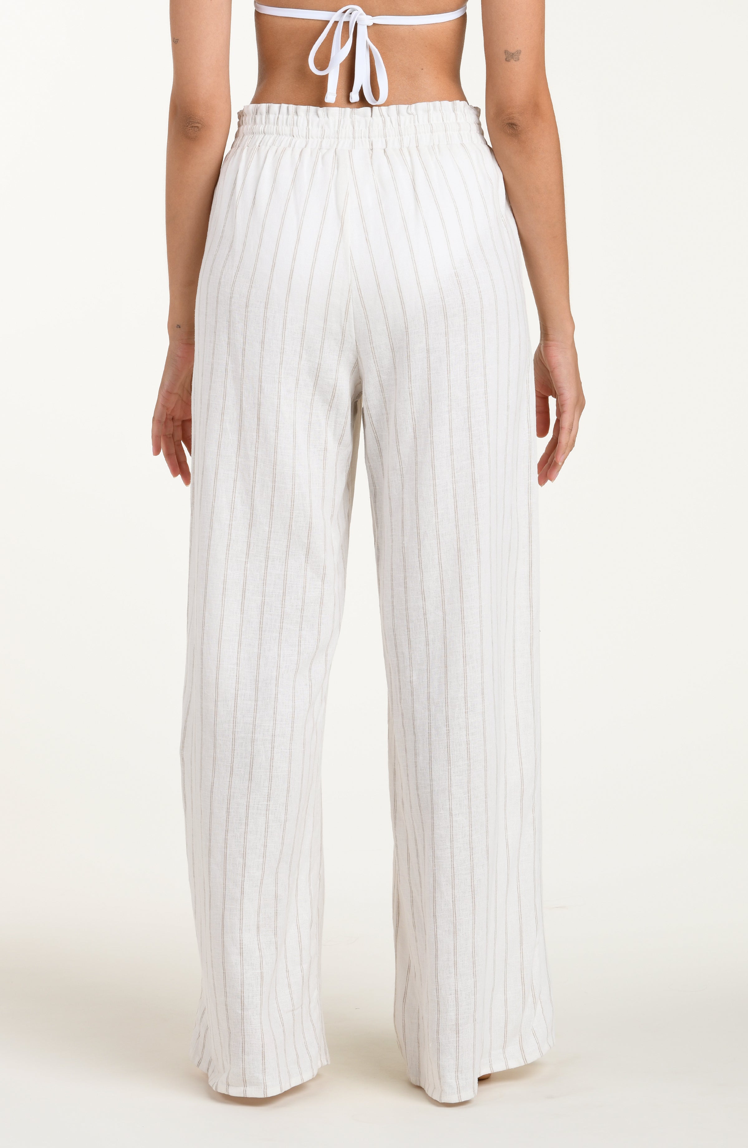 Back image of model wearing a cream striped colored wide-leg beach pants with a relaxed fit, drawstring waistband, and pockets. 