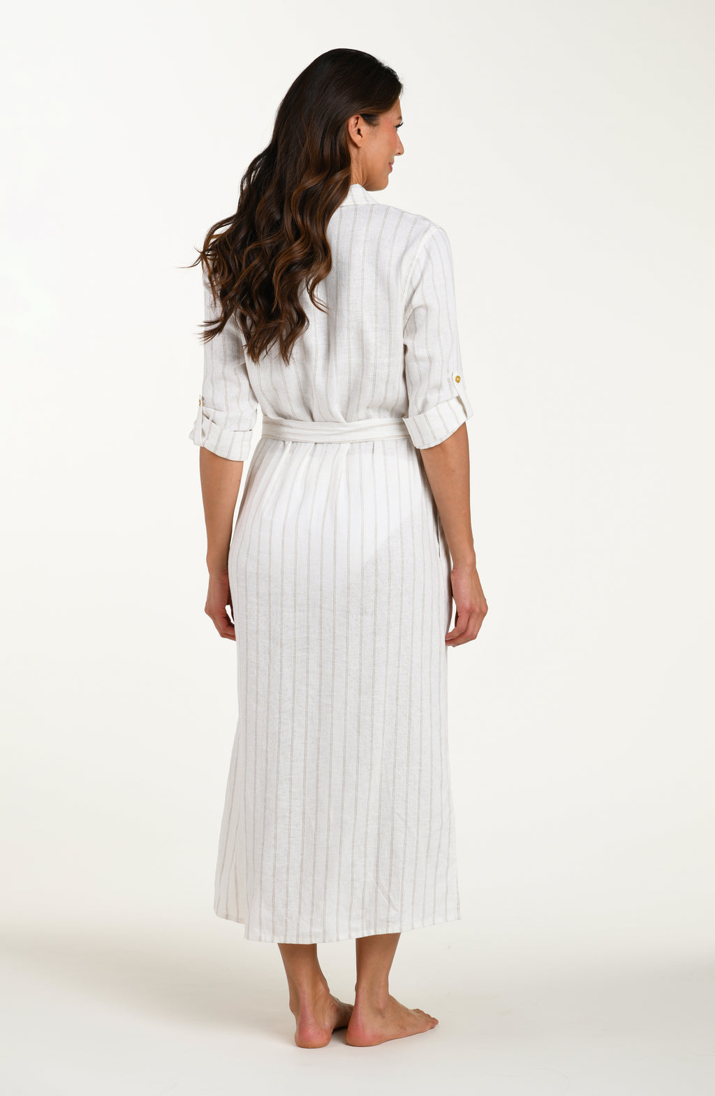 Full body back image of model wearing a cream striped colored shirt dress cover-up with roll-tab sleeves, a belted waist, and side slits. 