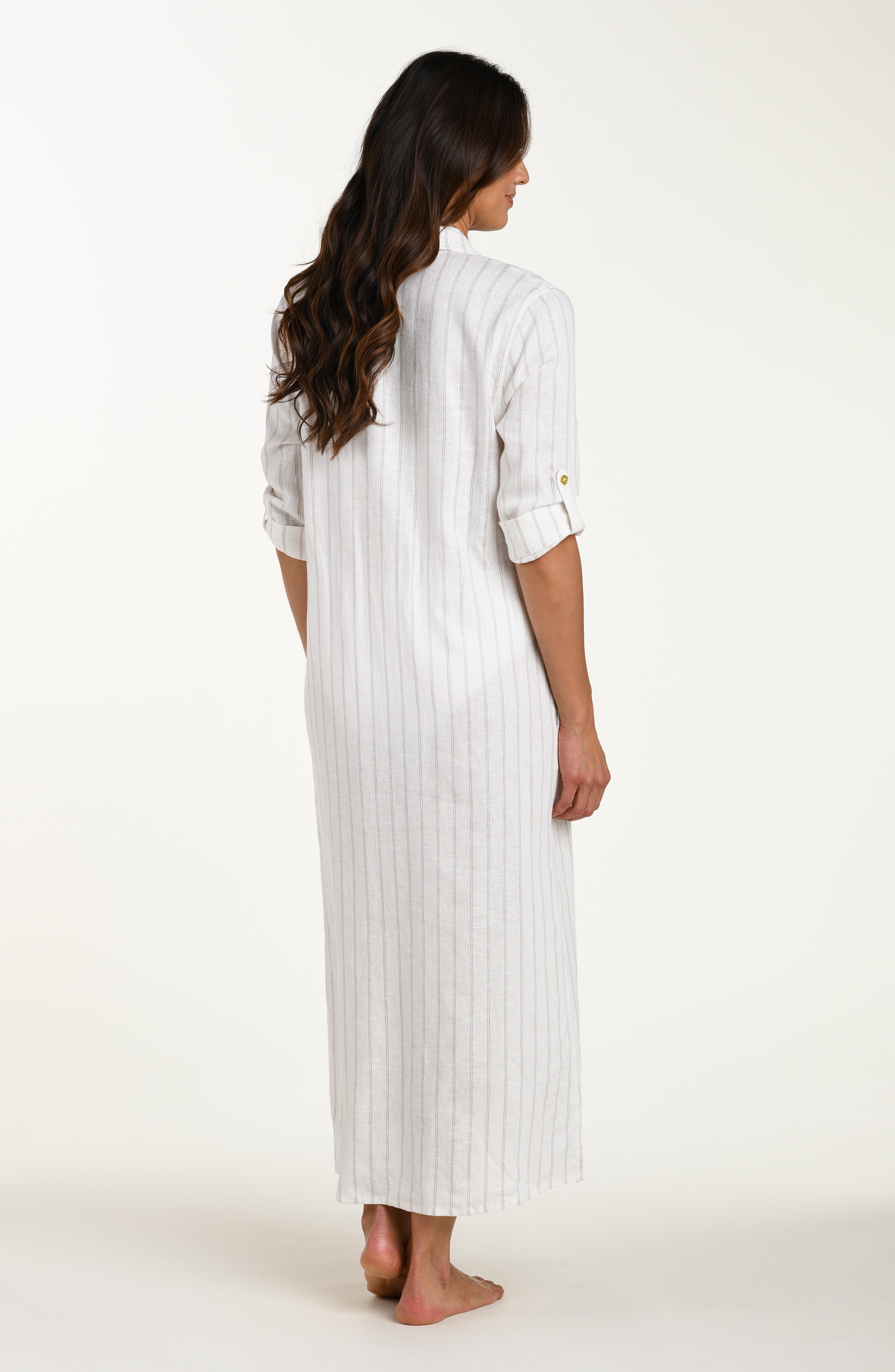 Full body back image of model wearing a cream striped colored shirt dress cover-up with roll-tab sleeves, a belted waist, and side slits. Model is showcasing cover up open without the belt. 