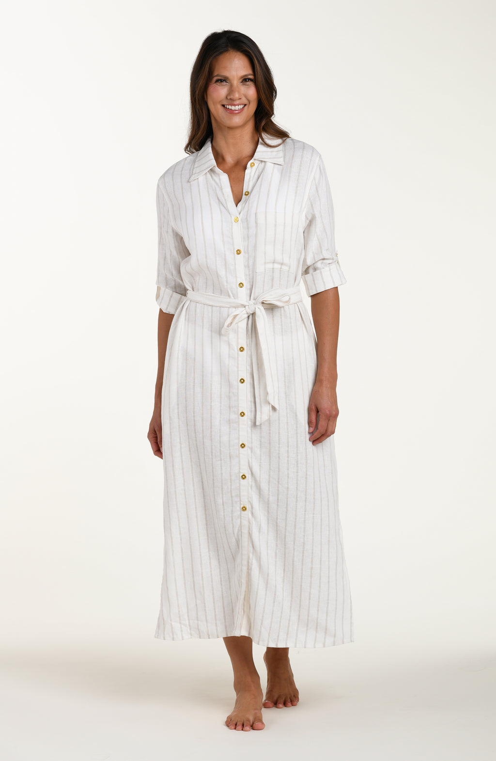 Full body front image of model wearing a cream striped colored button-down, shirt dress cover-up with roll-tab sleeves, a belted waist, and side slits. 