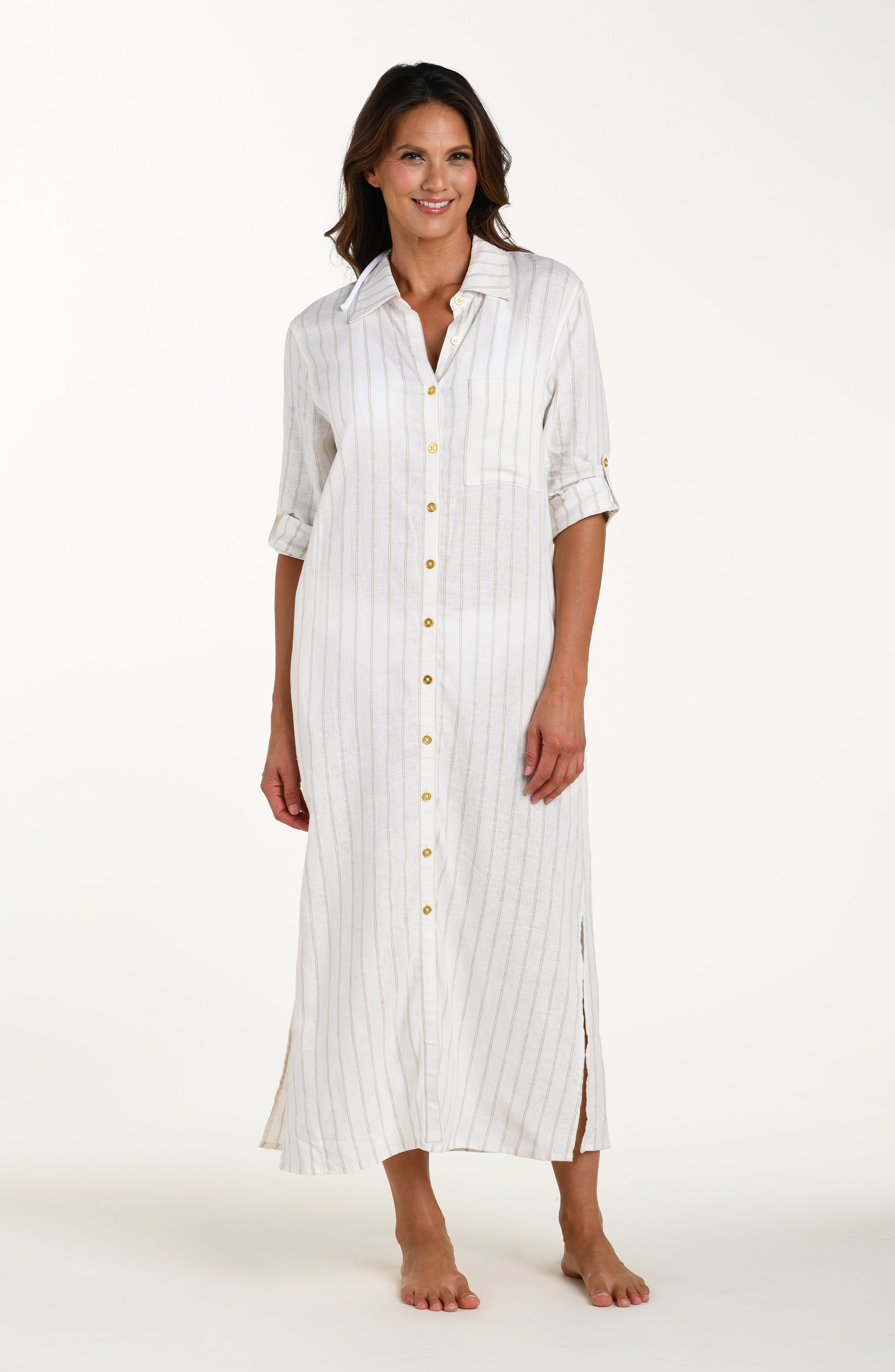 Full body front image of model wearing a cream striped colored button-down, shirt dress cover-up with roll-tab sleeves, a belted waist, and side slits. Model is showcasing cover up closed without the belt. 