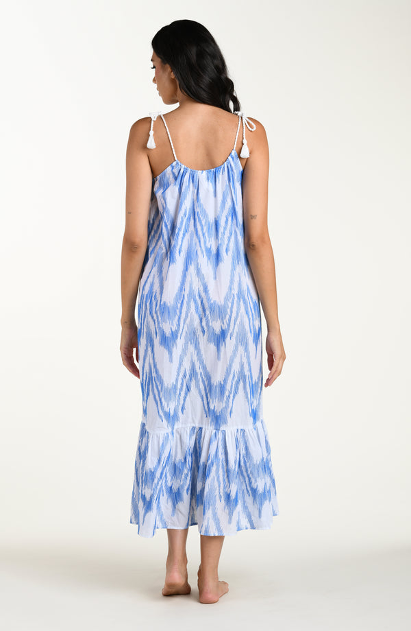 Full body back image of model wearing a light blue and white cover up dress featuring a maxi fit, loose flowy silhouette with adjustable shoulder ties for a customizable fit. 