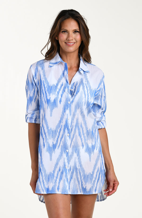 Front image of model wearing a light blue and white tunic cover-up featuring a relaxed, breezy fit with a button front, long sleeves and lightweight fabric that drapes. 