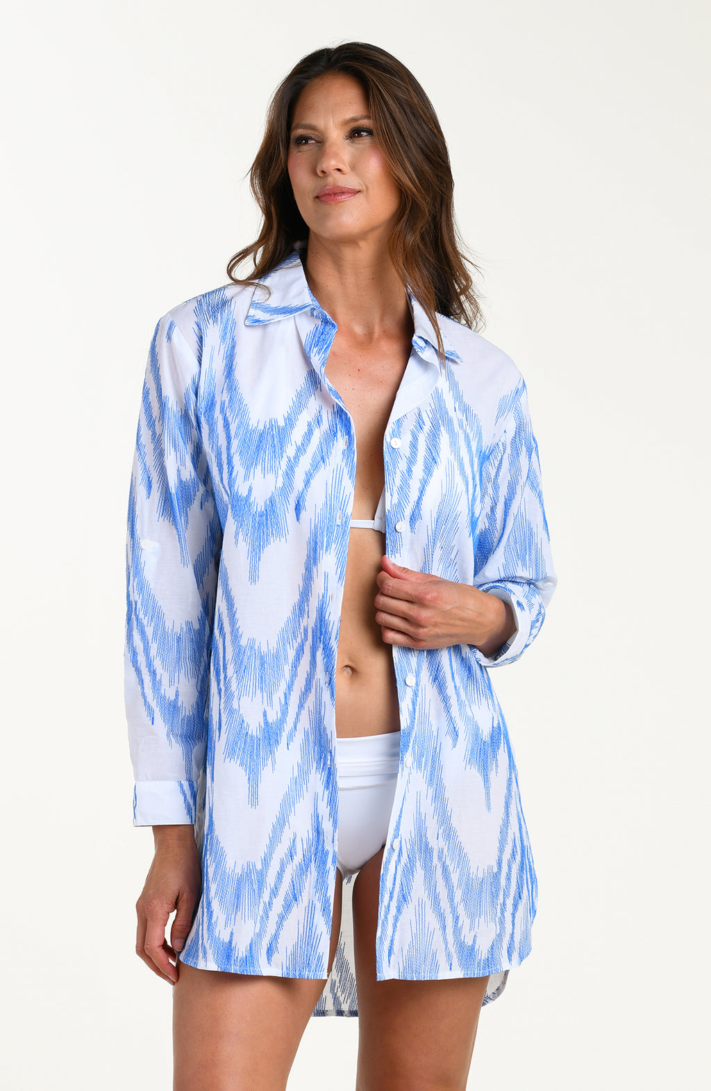 Front image of model wearing a light blue and white tunic cover-up featuring a relaxed, breezy fit with a button front, long sleeves and lightweight fabric that drapes. 