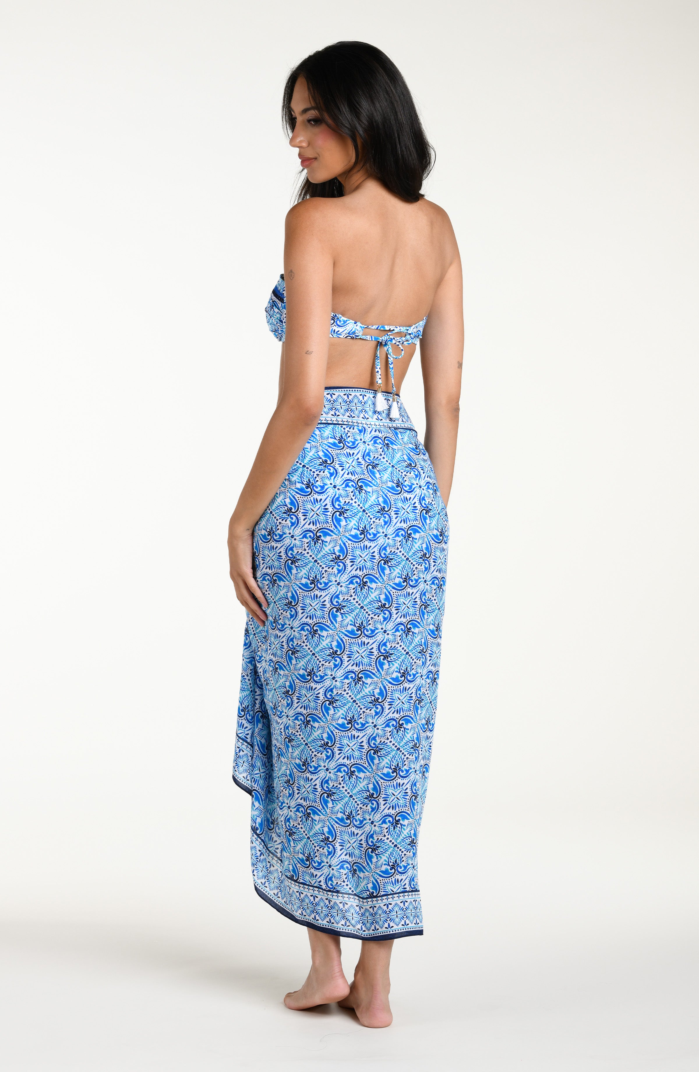 Woman wearing a blue floral patterned bikini top and matching sarong against a white background