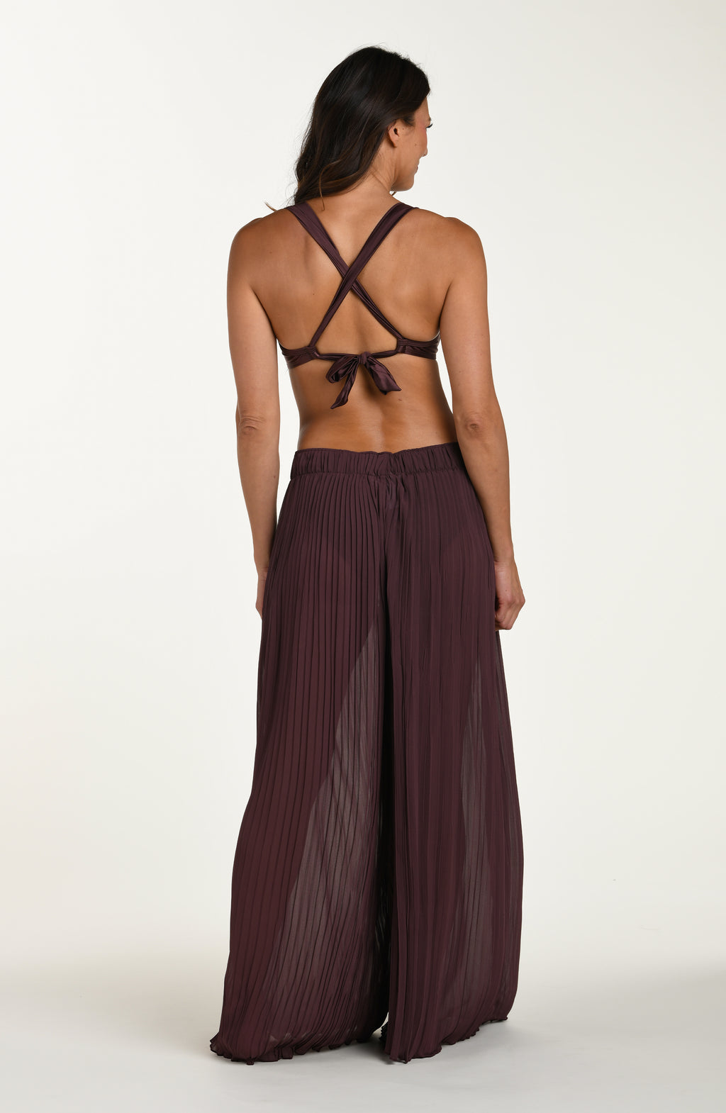 Woman wearing a burgundy strappy top and wide-leg pants on a white background