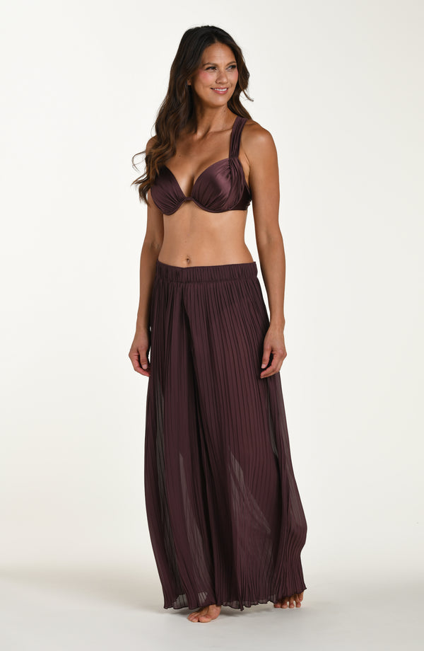 Woman wearing a dark purple bikini set with a matching skirt on a white background