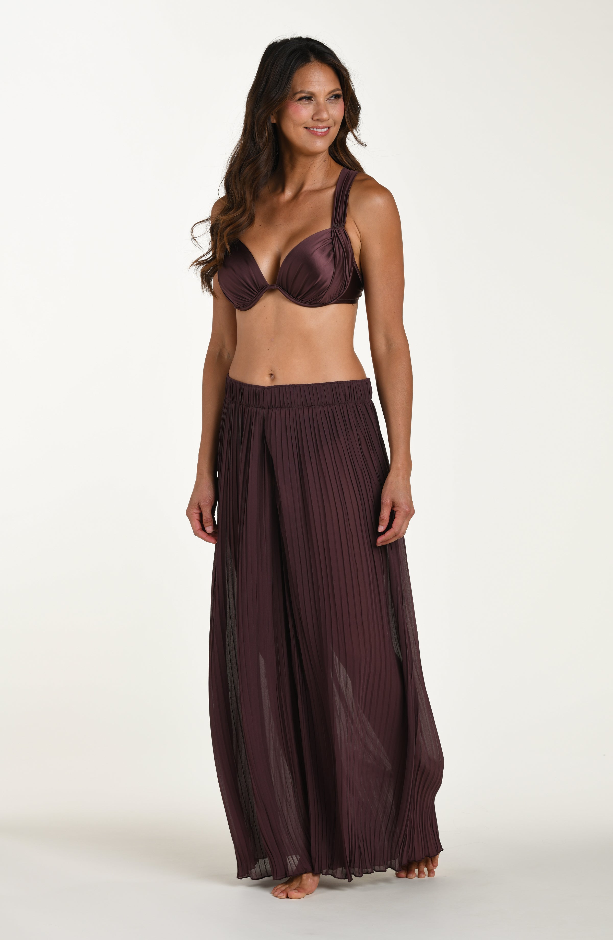 Woman wearing a dark purple bikini set with a matching skirt on a white background