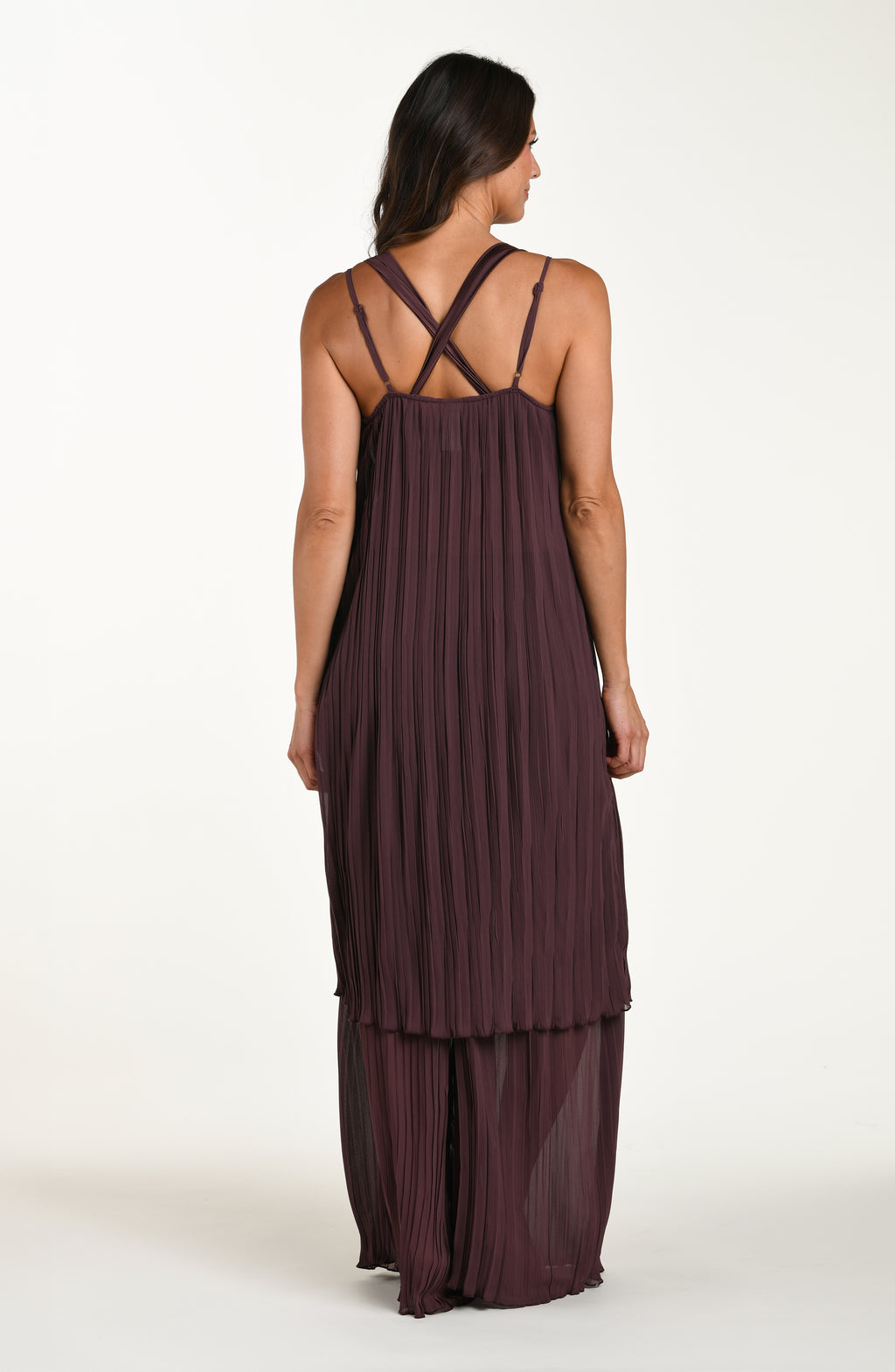 Woman wearing a brown pleated dress with criss-cross straps on a white background