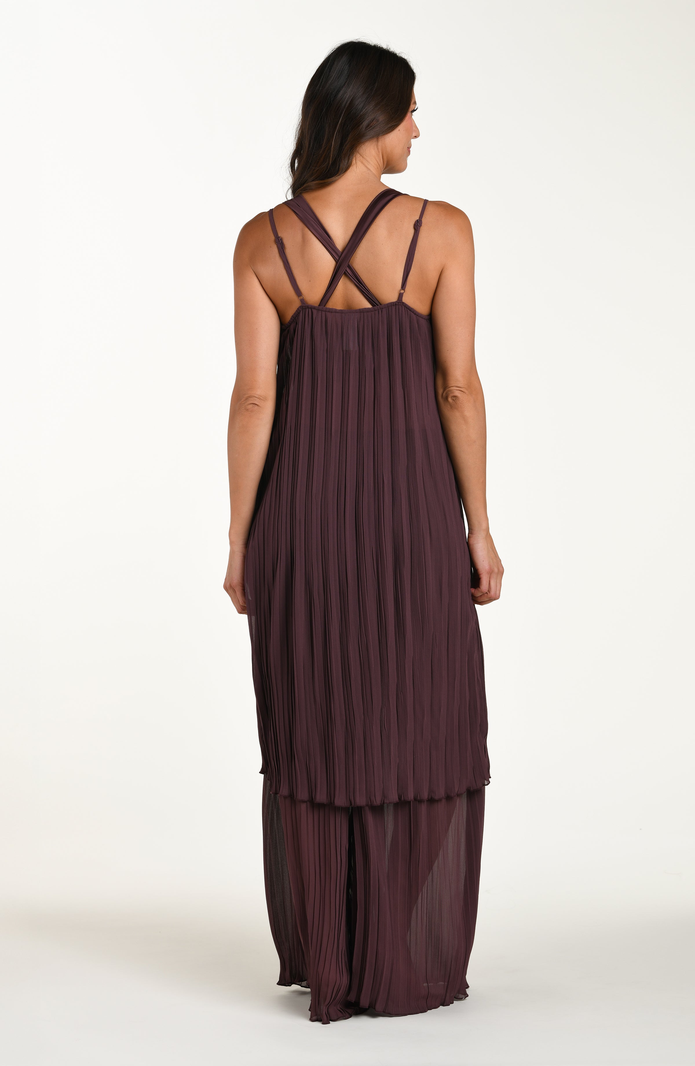 Woman wearing a brown pleated dress with criss-cross straps on a white background