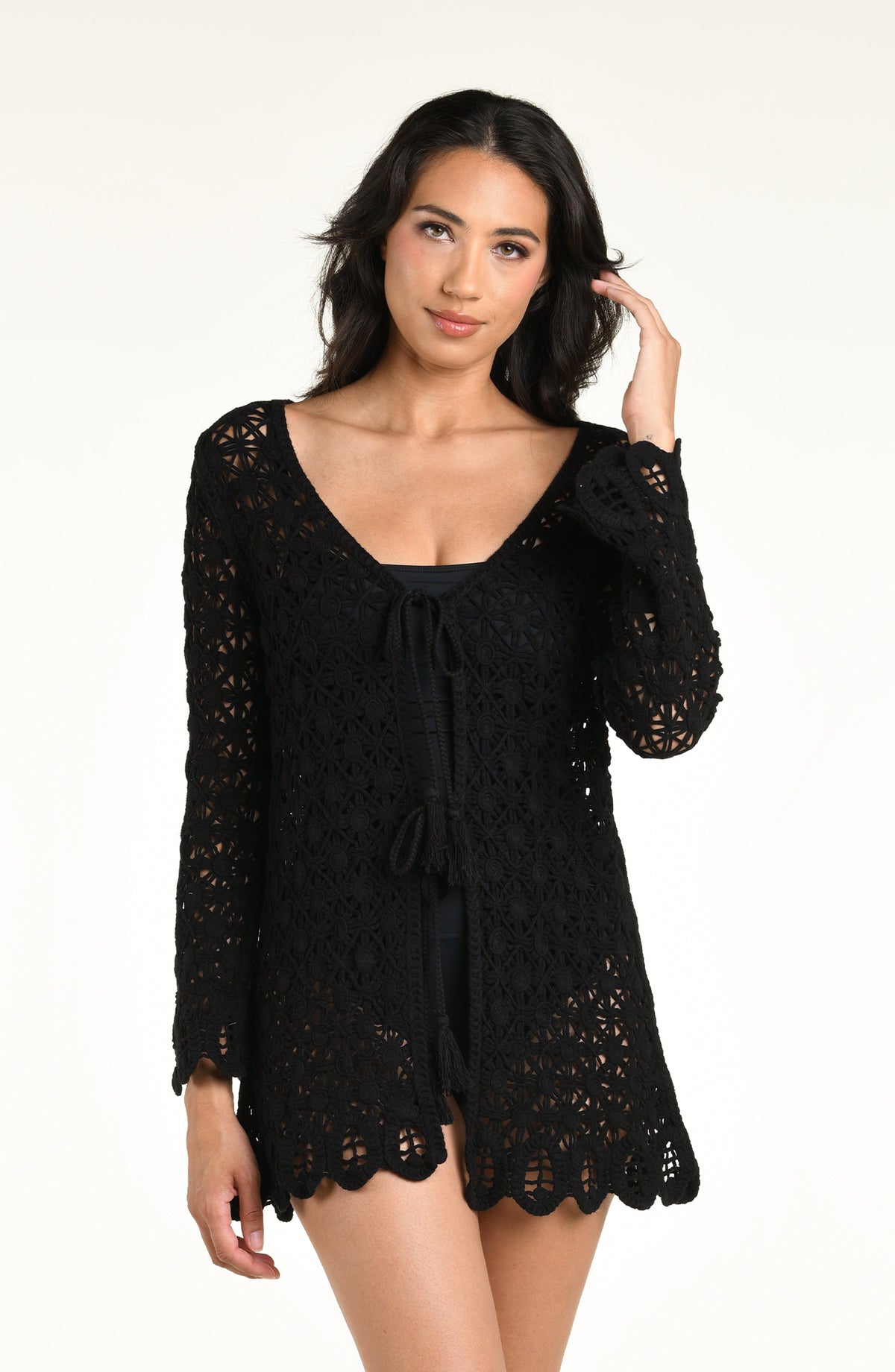 A woman modeling a black long-sleeve crochet kimono cover-up with a scalloped hem and front tie detail, photographed against a plain white studio background.