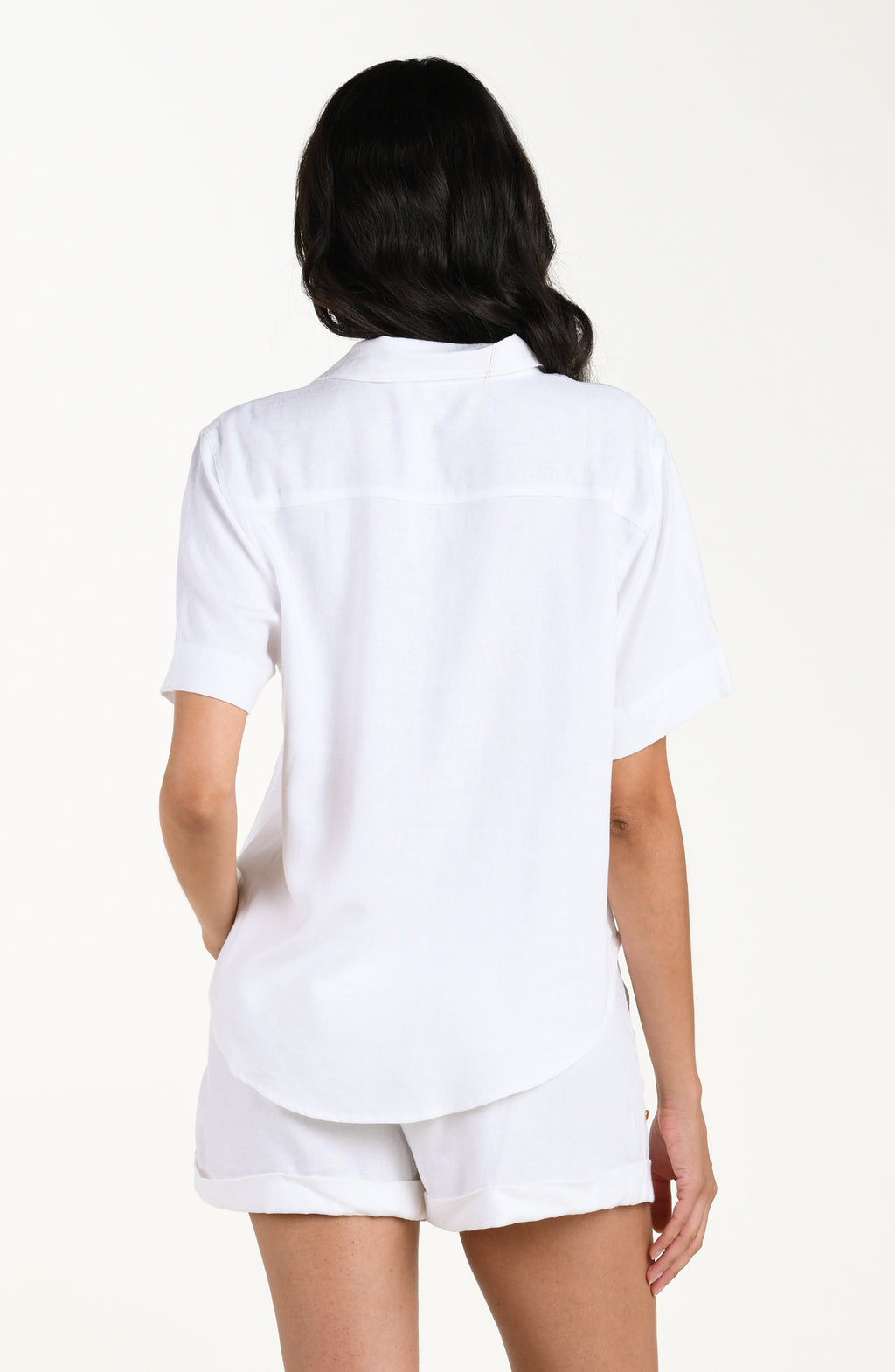 Back image of model wearing a white colored short-sleeve cover-up shirt with a relaxed fit and rounded hem. It's paired with matching beach shorts.
