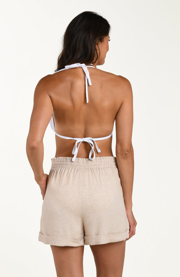 Back images of model wearing taupe colored beach shorts with an elastic waistband and cuffed hems. This is paired with a white bikini top. 