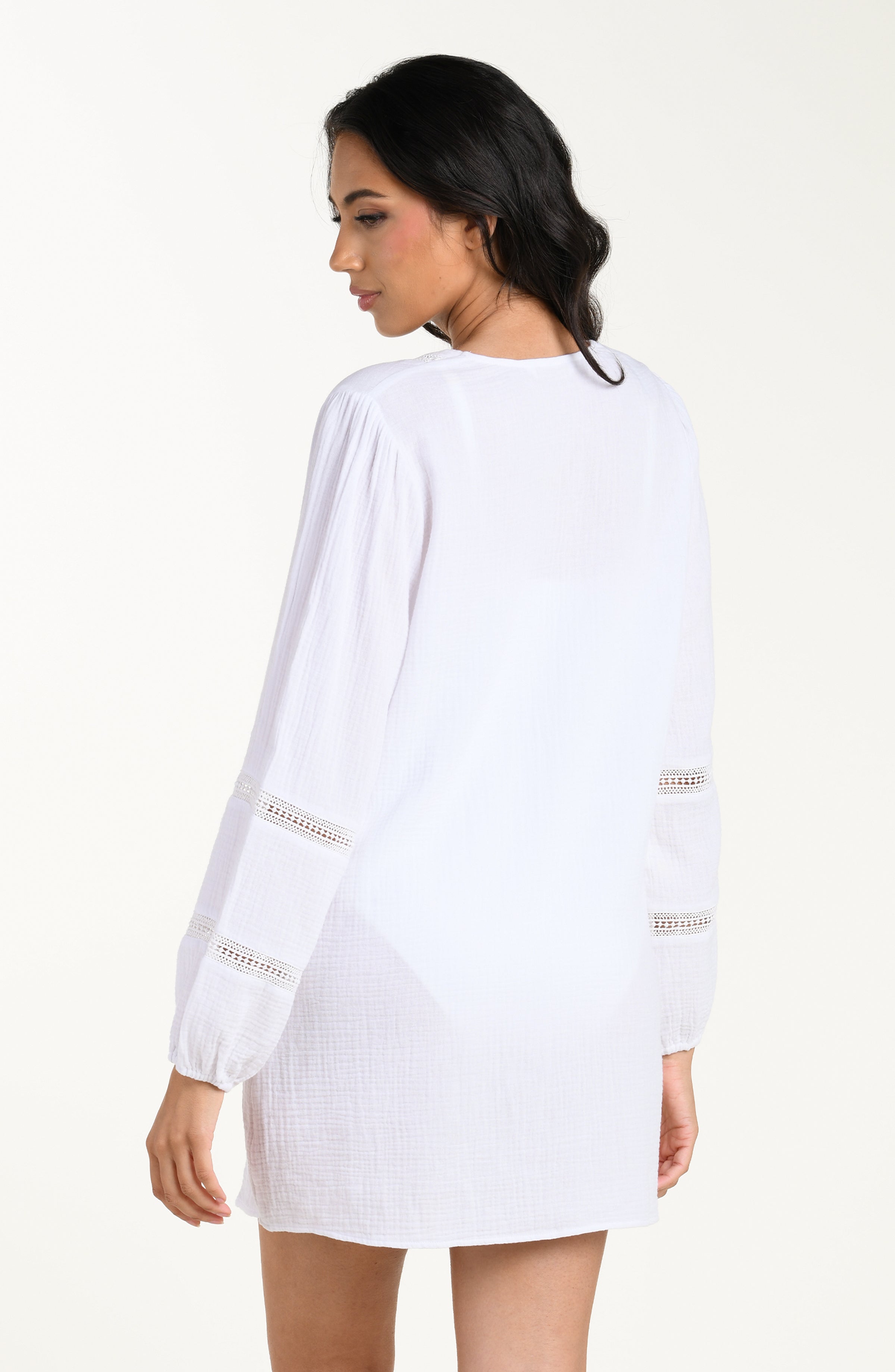 Back image of model wearing a white long-sleeve tunic cover-up with sheer lace trim accents on the sleeves.