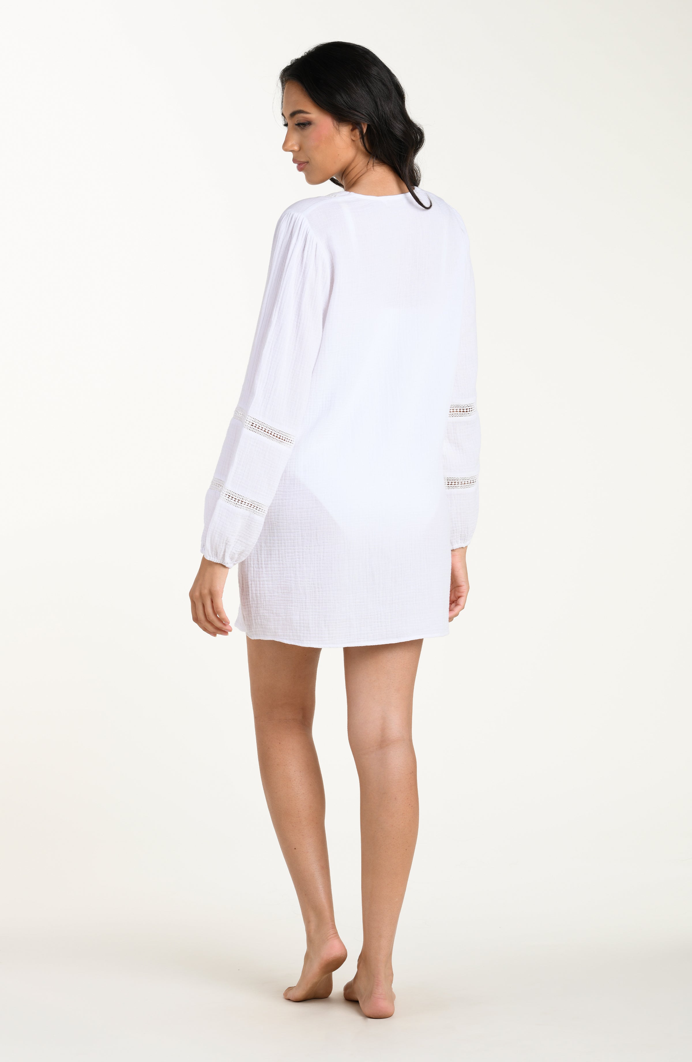 Full body back image of model wearing a white long-sleeve tunic cover-up with sheer lace trim accents on the sleeves.