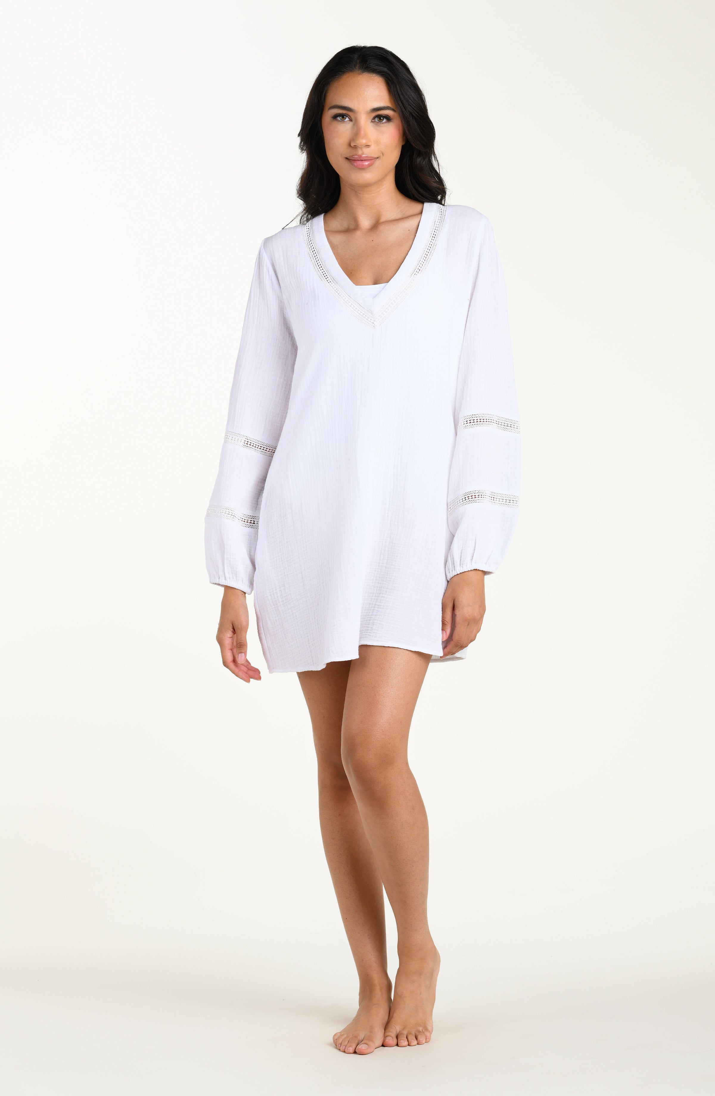 Full body front image of model wearing a white long-sleeve tunic cover-up with a V-neckline and sheer lace trim accents. 