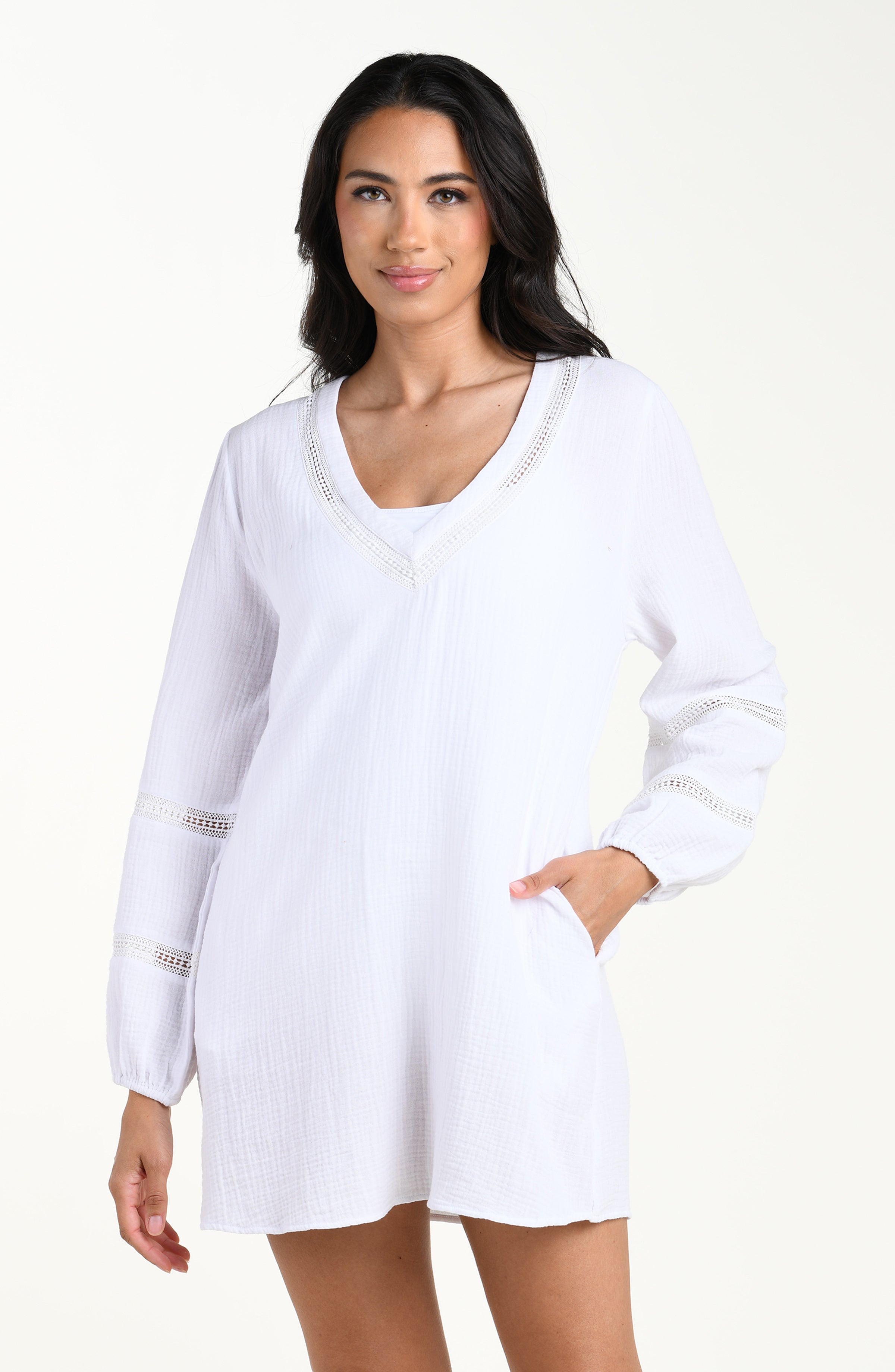 Front image of model wearing a white long-sleeve tunic cover-up with a V-neckline and sheer lace trim accents. 