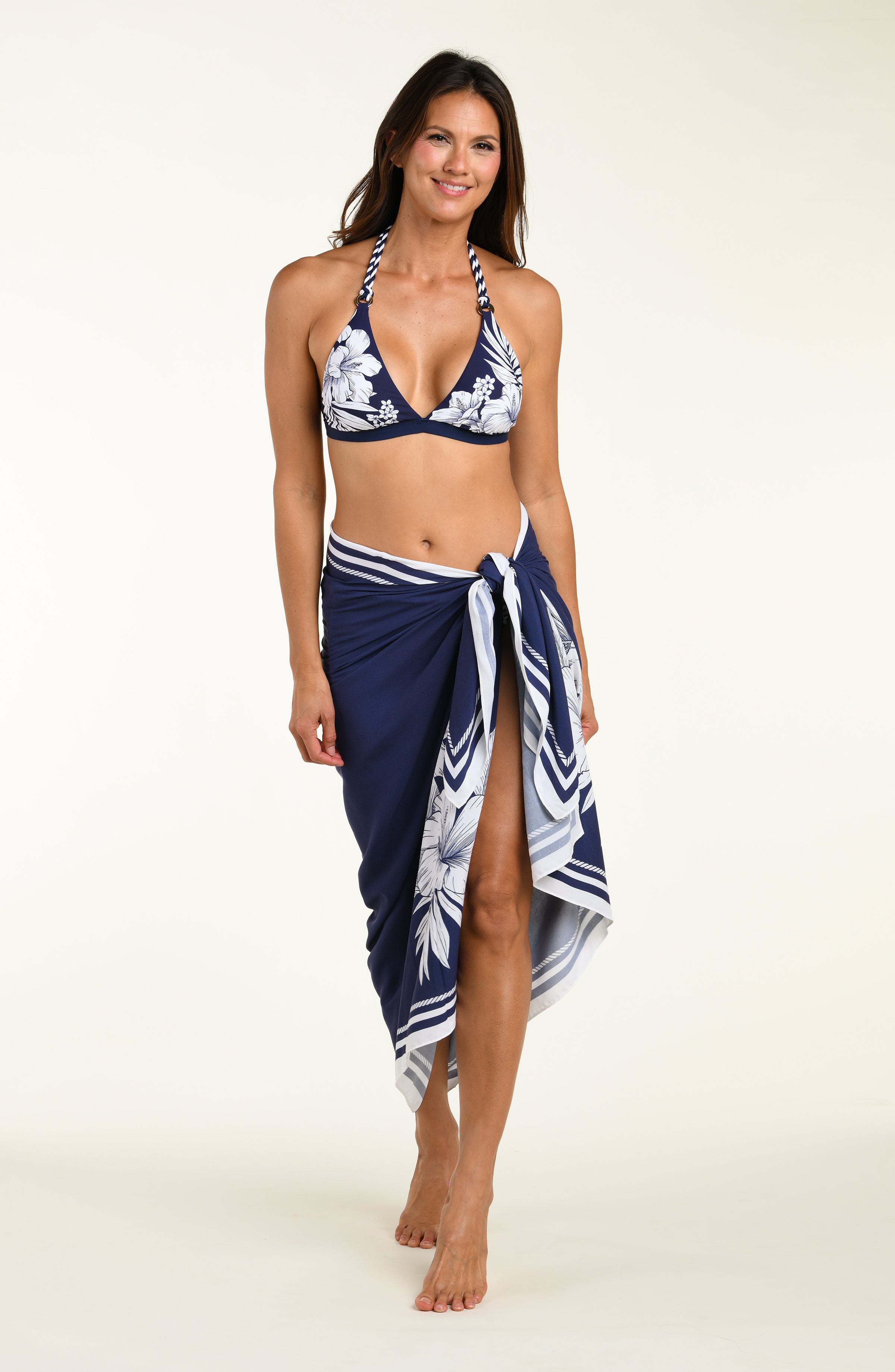 Person wearing a navy blue sarong with white floral patterns and a matching bikini top on a white background