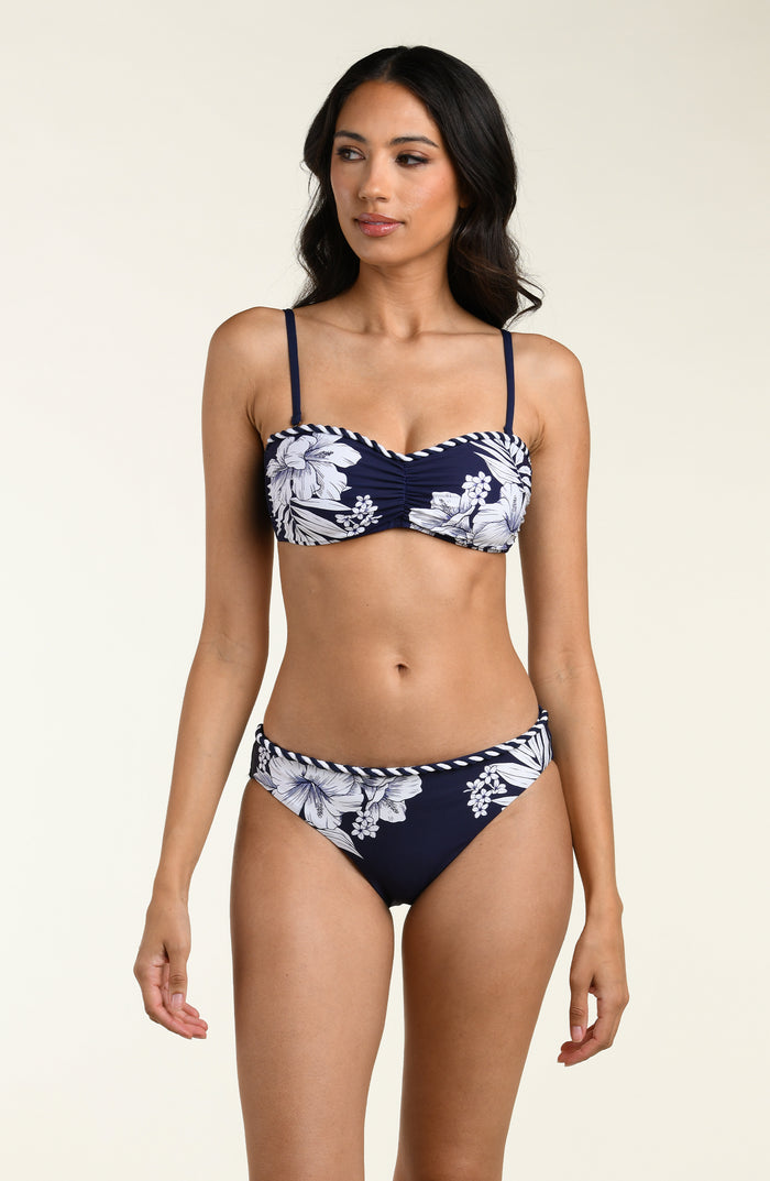 Woman wearing a navy blue and white floral bikini top and matching bottom against a beige background