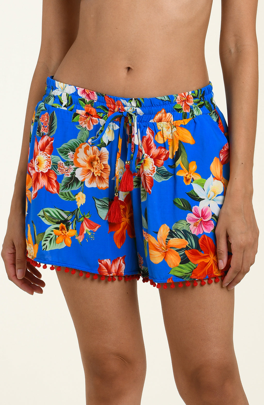 Woman wearing colorful floral shorts with pom-pom trim on a neutral background