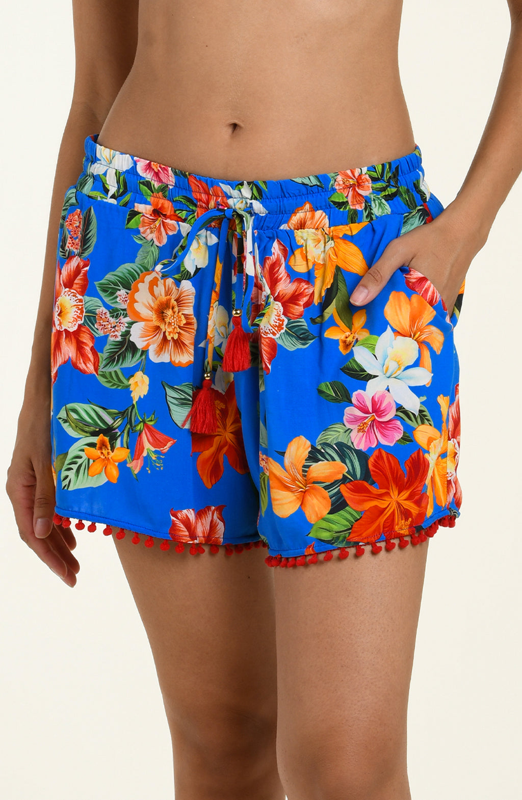 Woman wearing colorful floral shorts with pom-pom trim on a neutral background