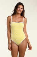 Woman wearing a yellow patterned one piece swimsuit on a beige background