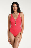 Woman wearing a guava colored one piece swimsuit against a white background. 