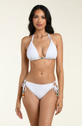 Woman wearing a white bikini top and matching bikini bottom on a beige background