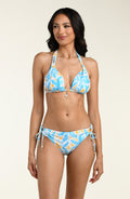Woman wearing a blue and yellow patterned bikini top and matching bikini bottom against a beige background