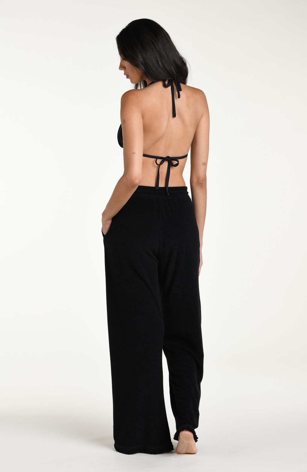 Woman wearing a black bikini top and black beach pants against a white background
