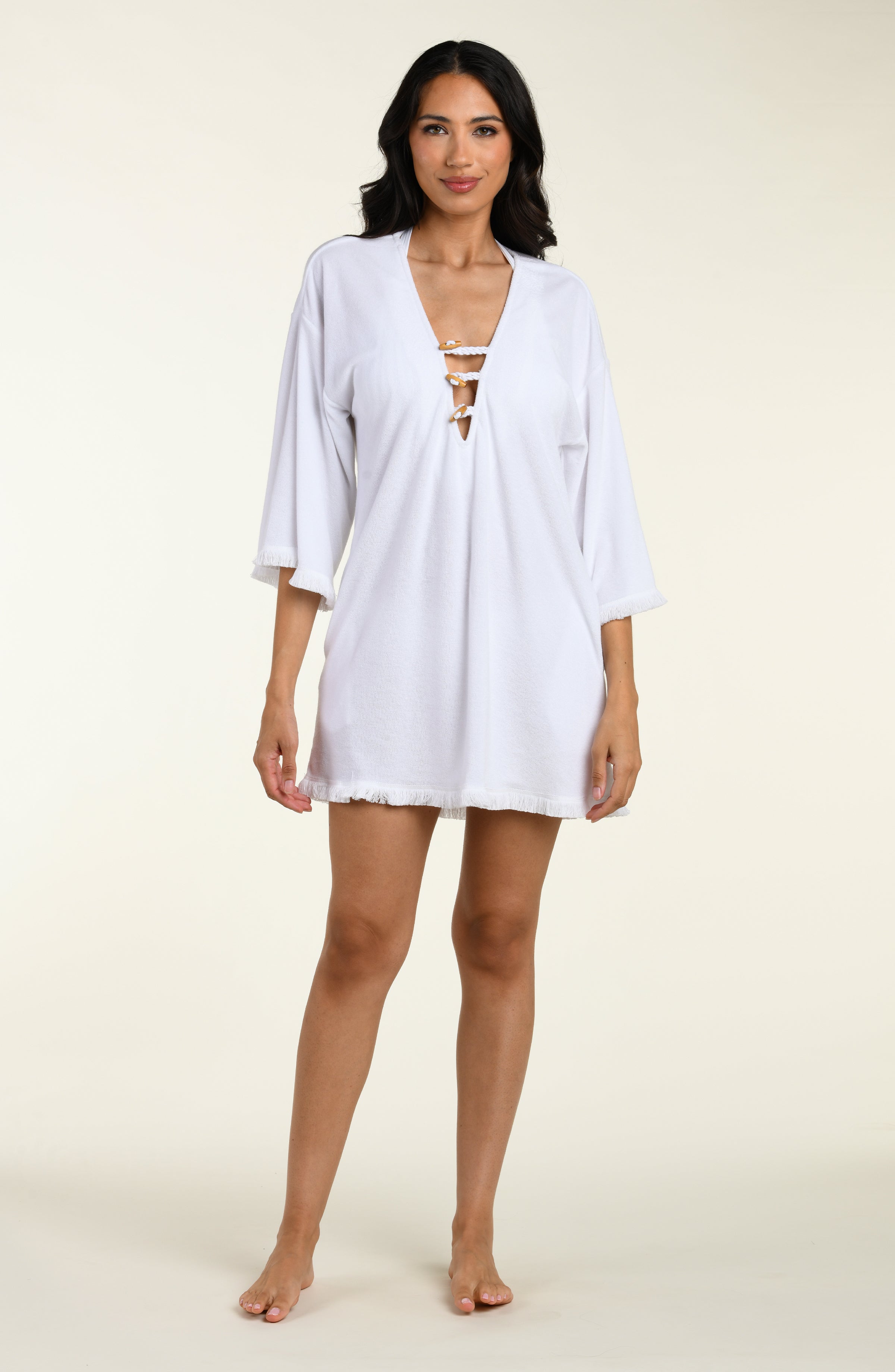 Woman wearing a white cover-up tunic  with lace-up front on a beige background