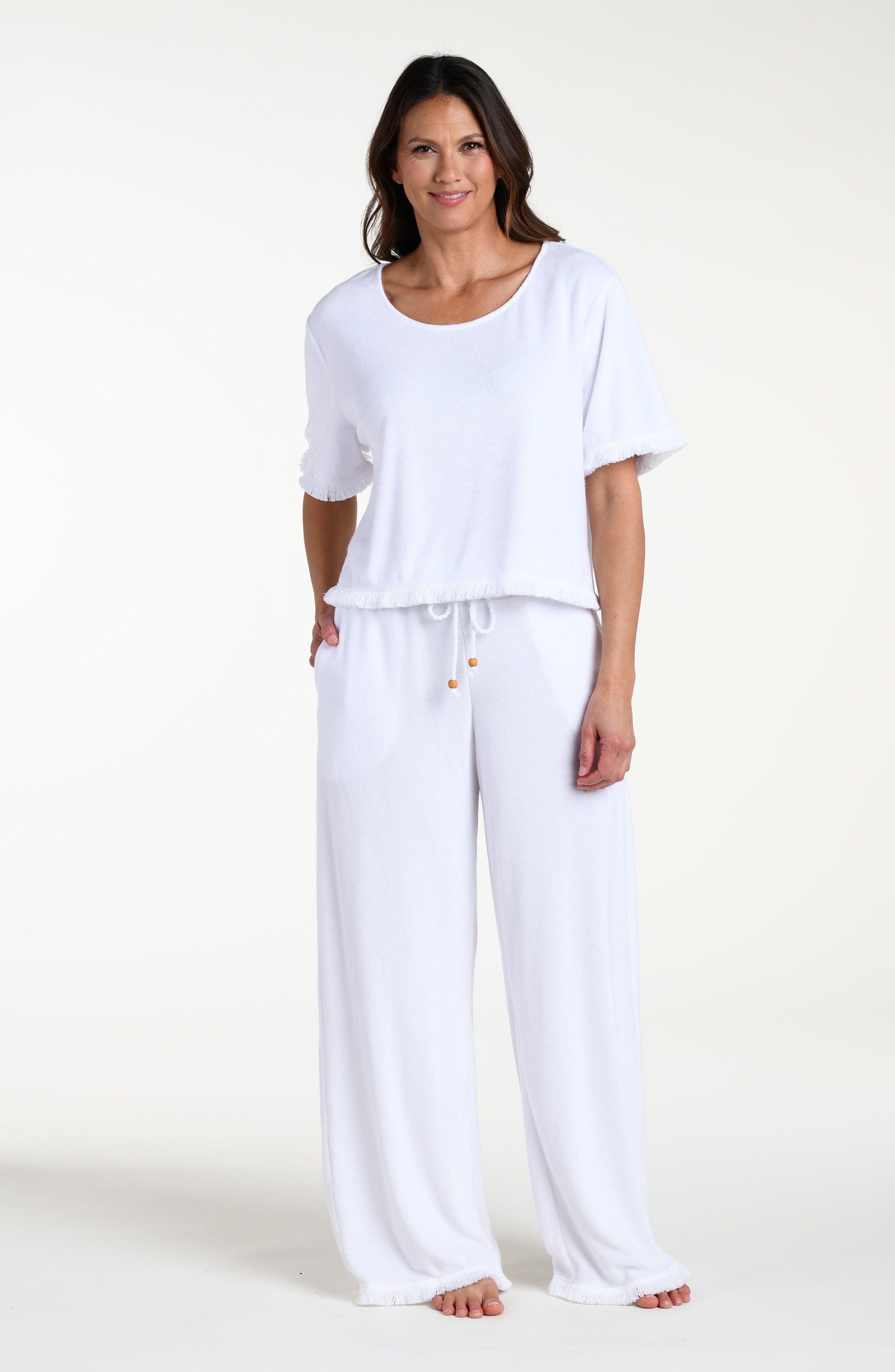 Woman wearing a white short sleeve top and matching beach pants against a white background