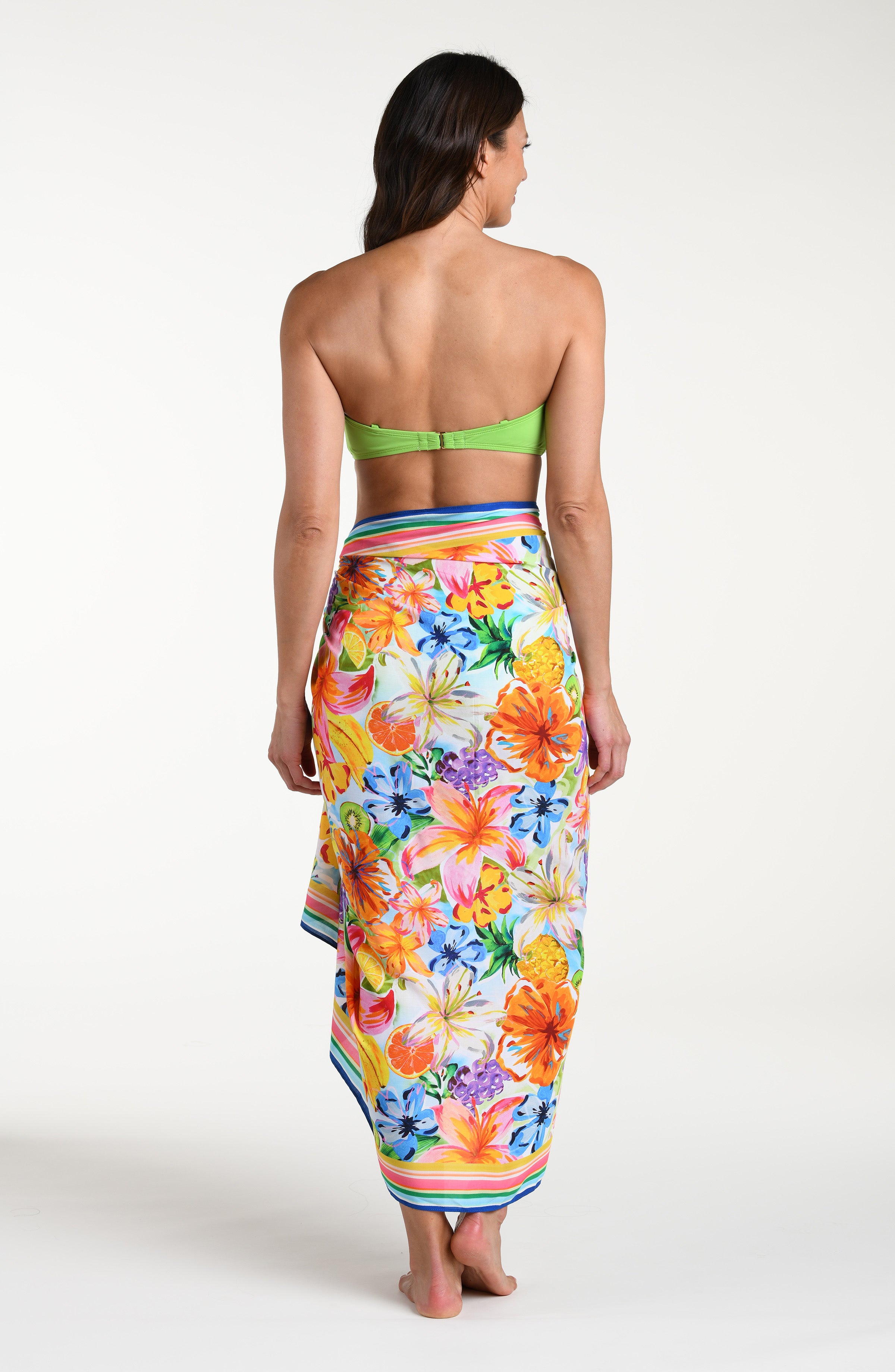 Woman wearing a green bikini top and colorful tropical pareo wrap against a white background.