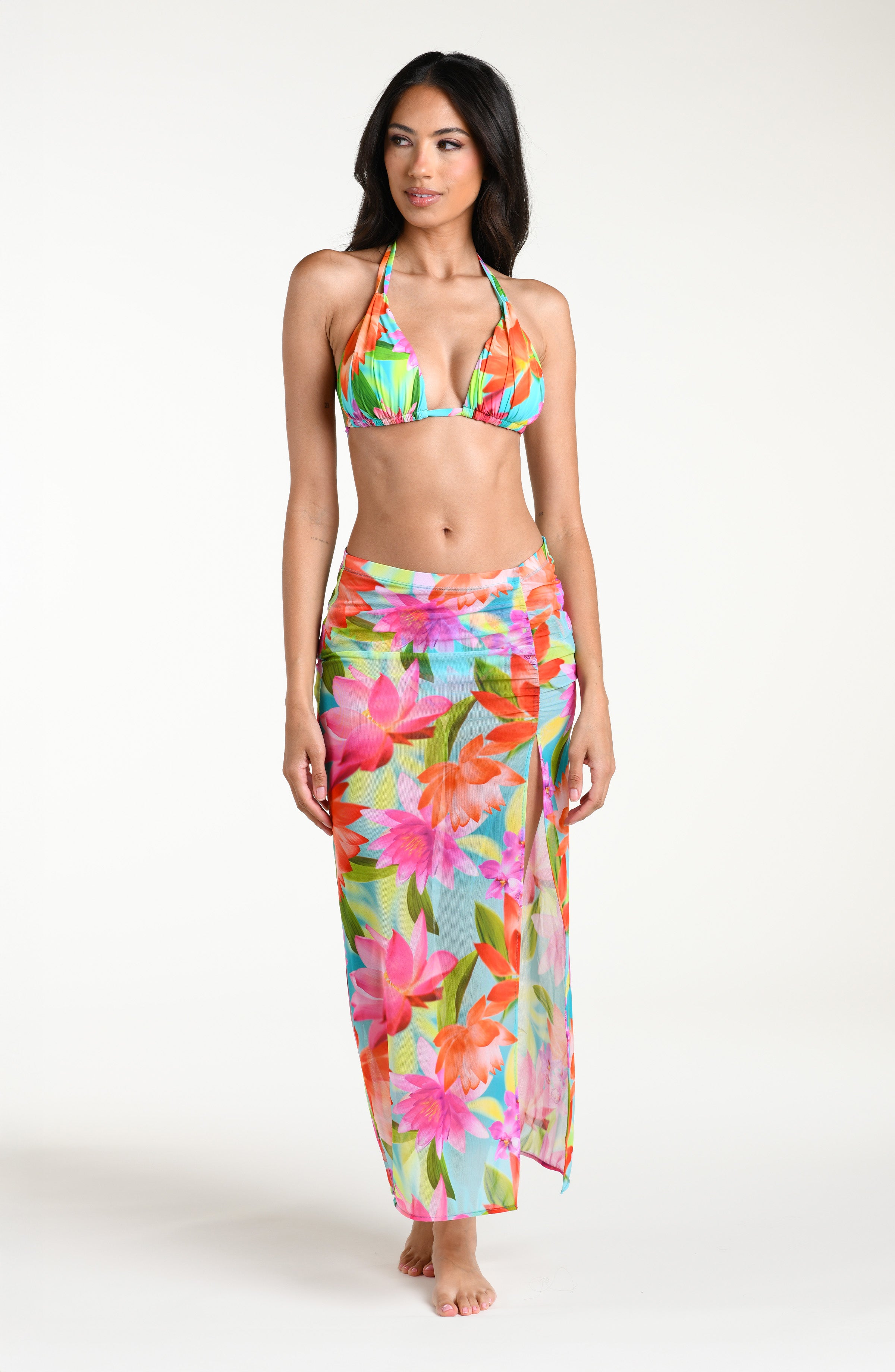 Woman wearing a bright floral bikini top and matching midi skirt cover up against a white background.