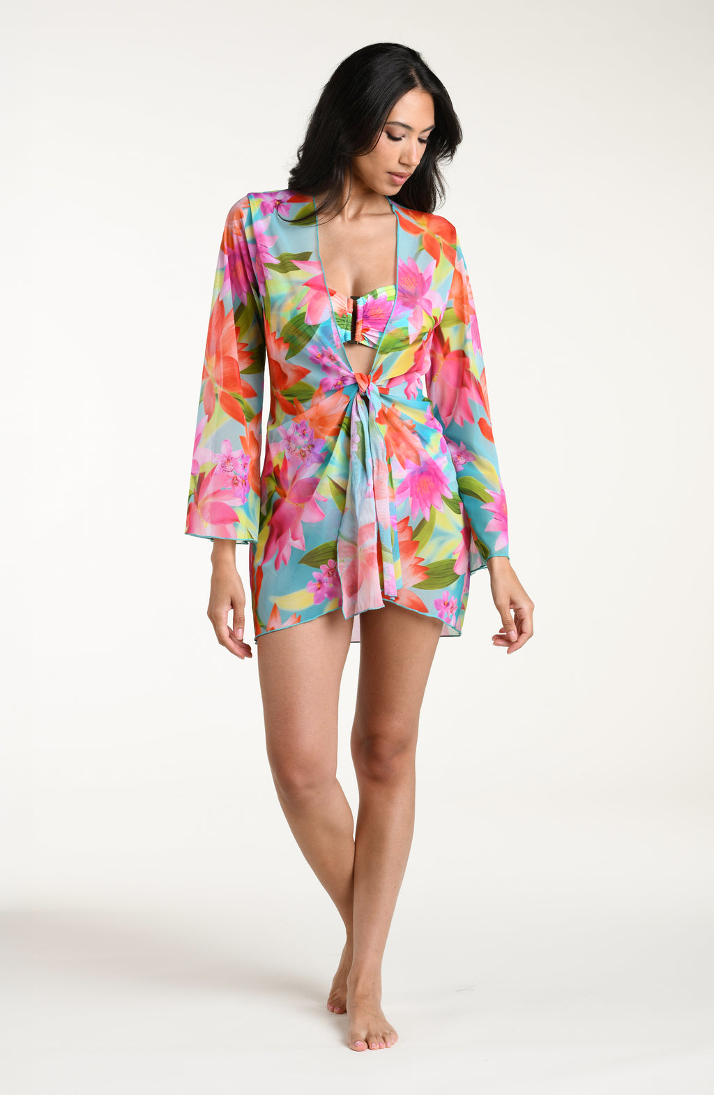 Woman wearing a bright floral kimono cover up with a matching bikini underneath, against a white background.