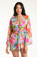 Woman wearing a bright floral kimono cover up with a matching bikini underneath, against a white background.