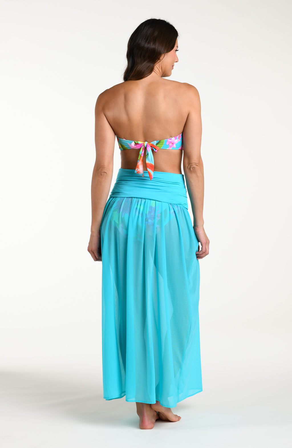 Woman wearing a turquoise skirt and a bright floral bikini top against a white background.