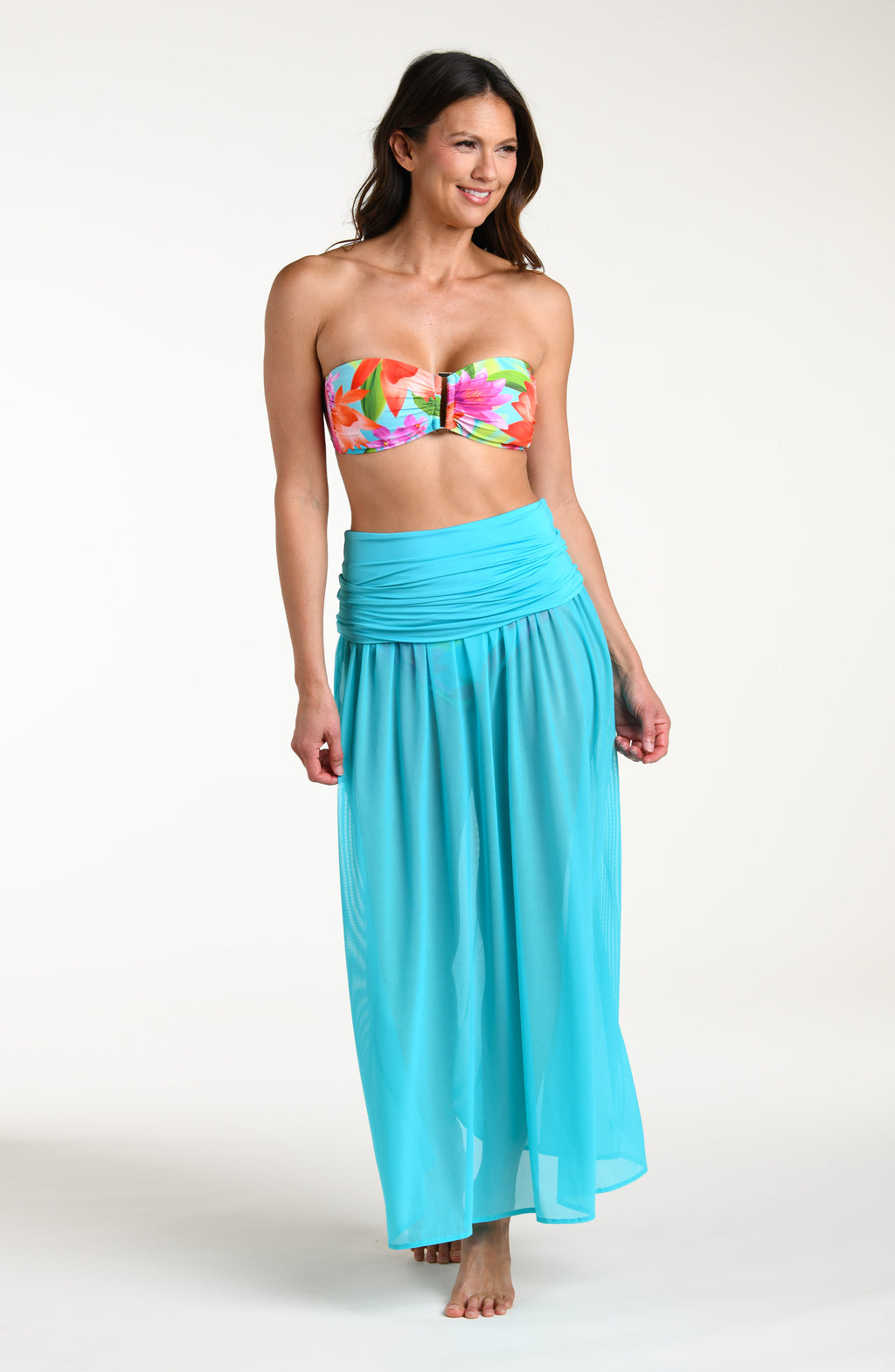 Woman wearing a turquoise skirt and a bright floral bikini top against a white background.