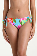 Woman wearing a bright floral side tie bikini bottom against a white background
