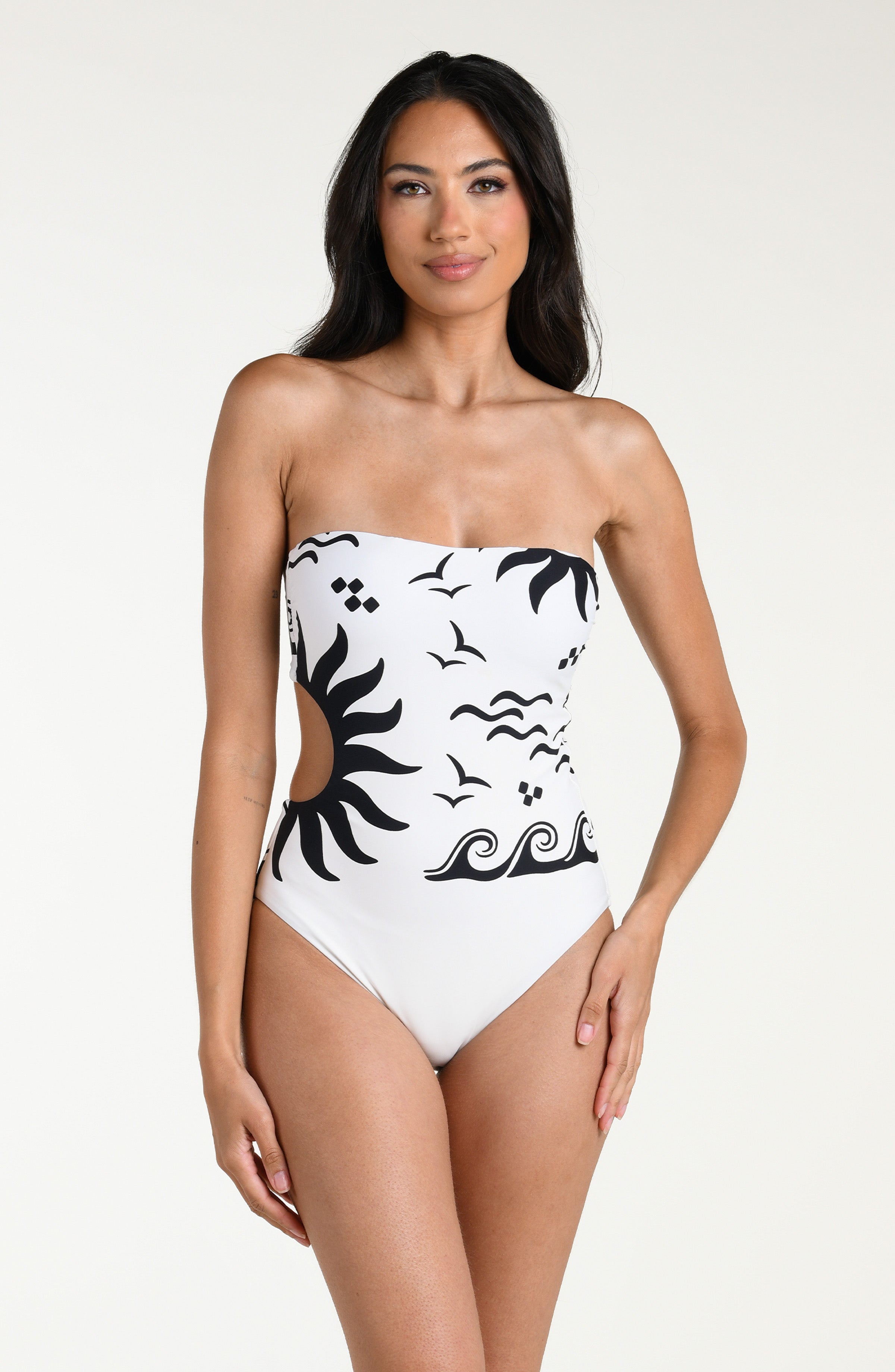 Woman wearing a white bandeau one piece swimsuit with black designs on a white background. 