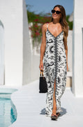 Woman wearing a black and white maxi dress walking next to a pool outdoors. 