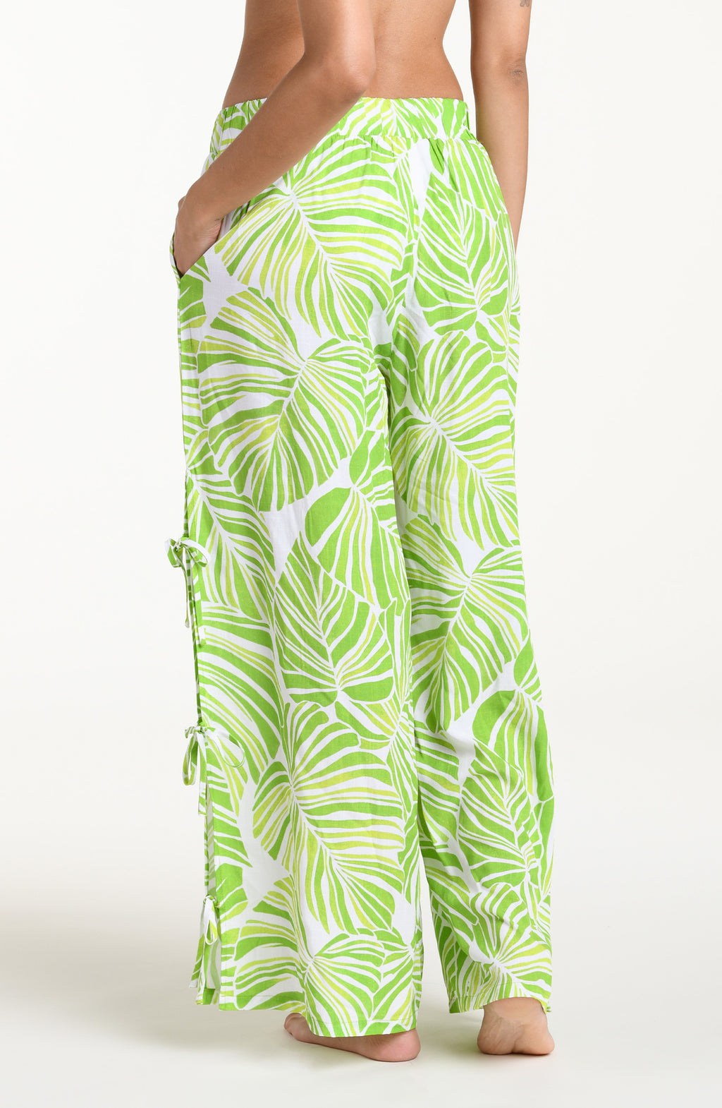 Woman wearing a green and white leaf-patterned beach pants against a white background