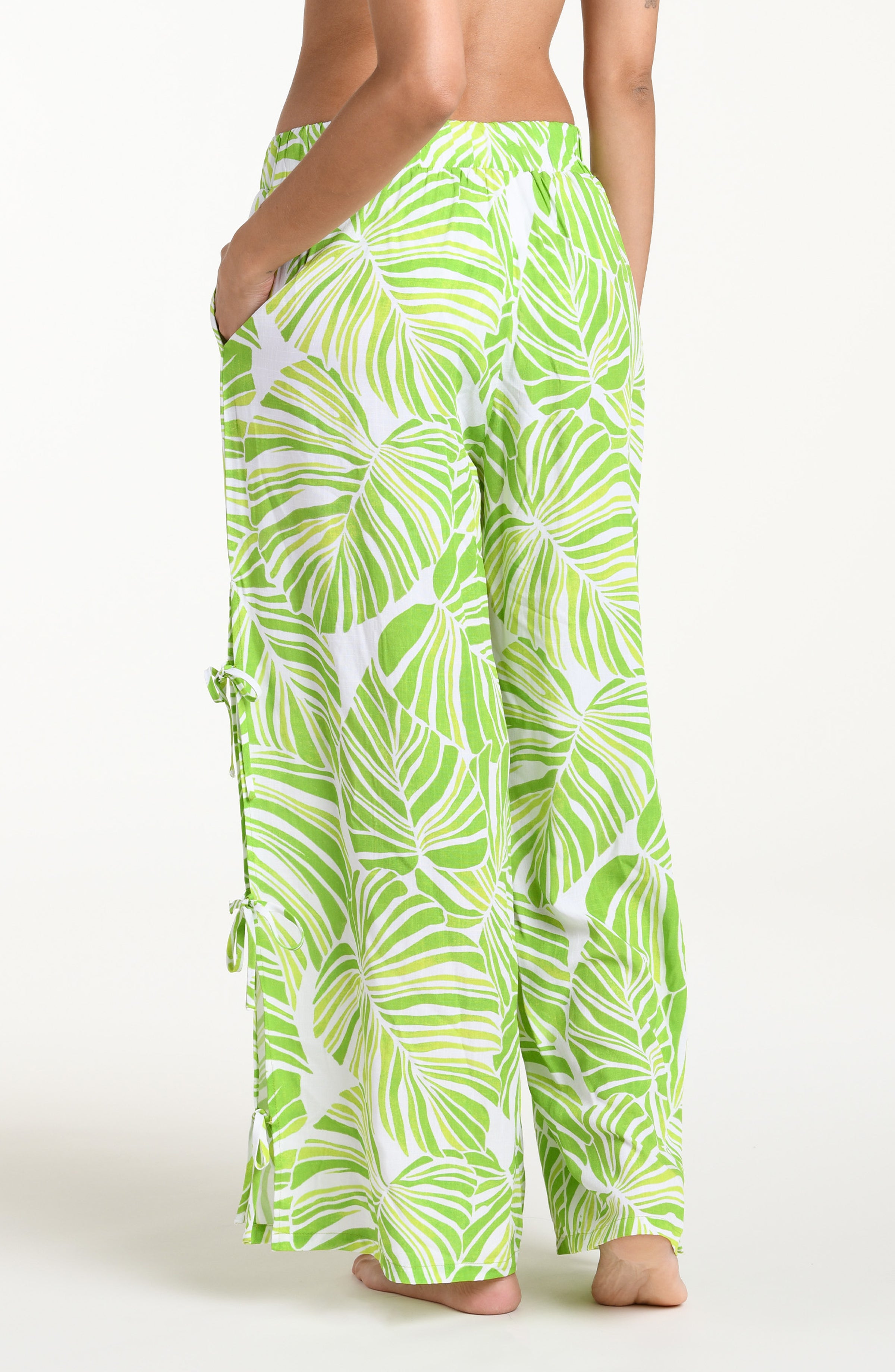 Woman wearing a green and white leaf-patterned beach pants against a white background