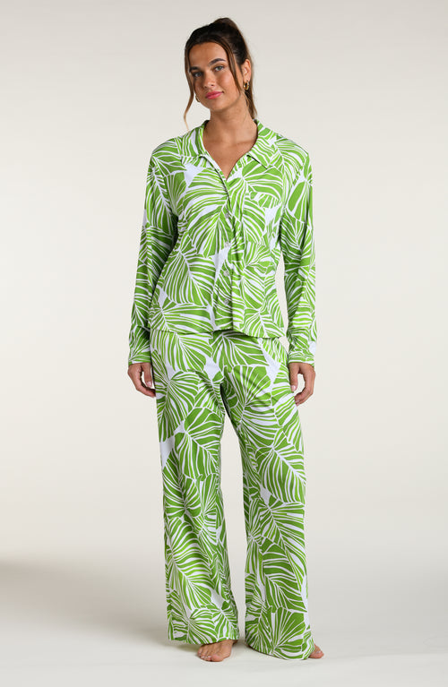 Woman wearing a green and white leaf-patterned pajama pant set against a plain white background.