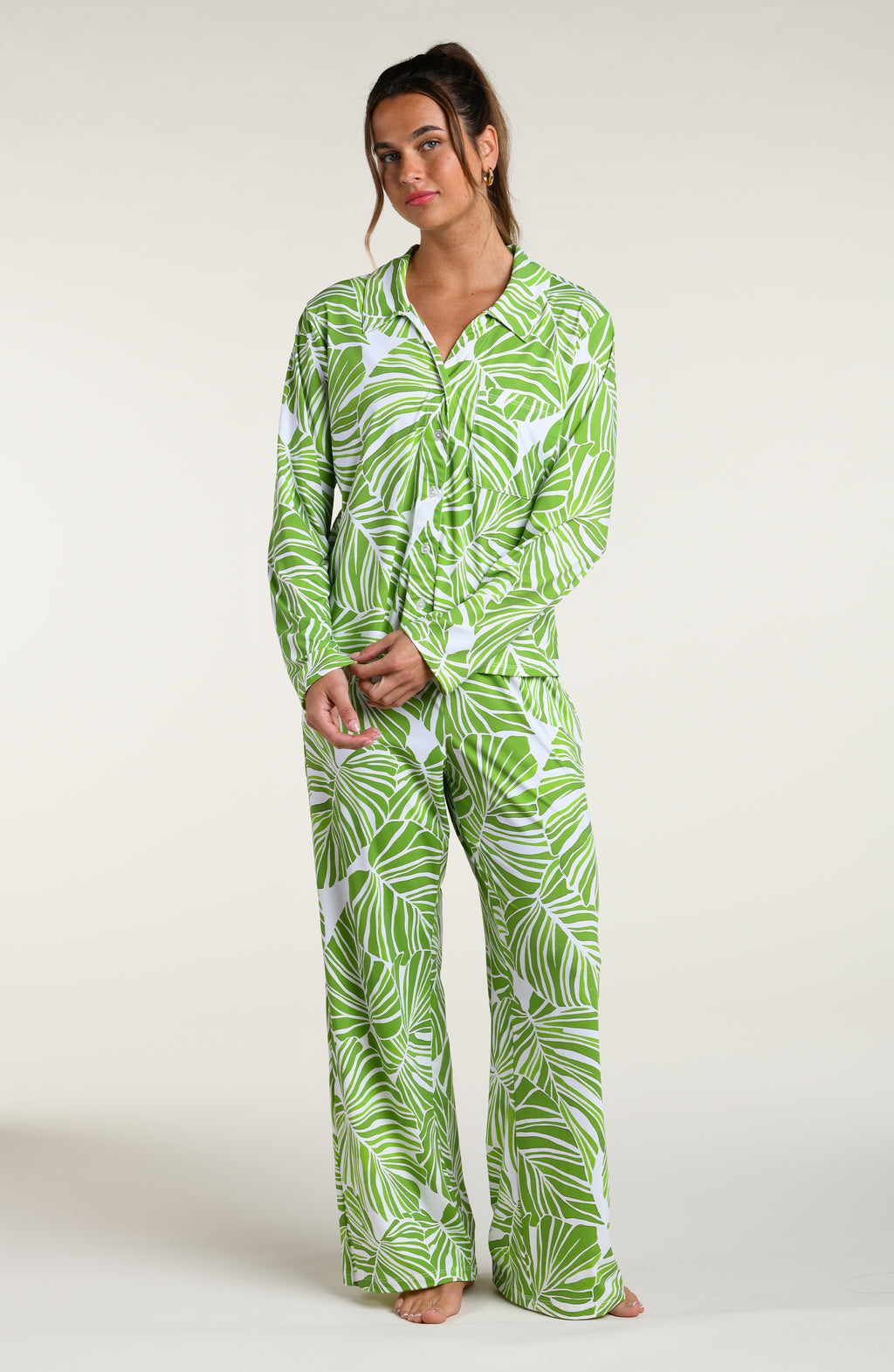 Woman wearing a green and white leaf-patterned pajama pant set against a plain white background.
